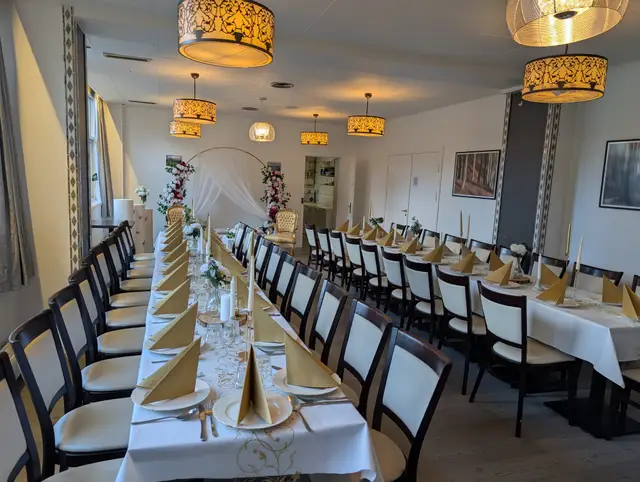 A long table with fan-folded gold napkins leading to a white draped arch with flowers