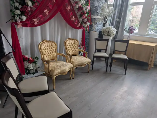 Two gilded armchairs for the couple in front of a red draped backdrop with white flowers