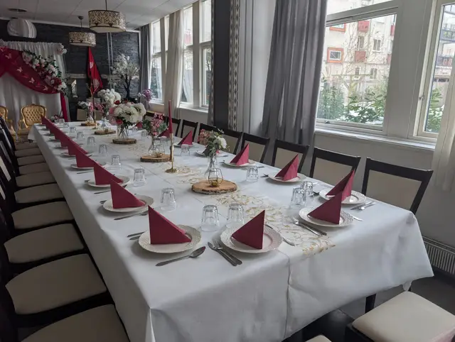 A long table with red napkins, white floral arrangements and wooden slices, lit by the windows