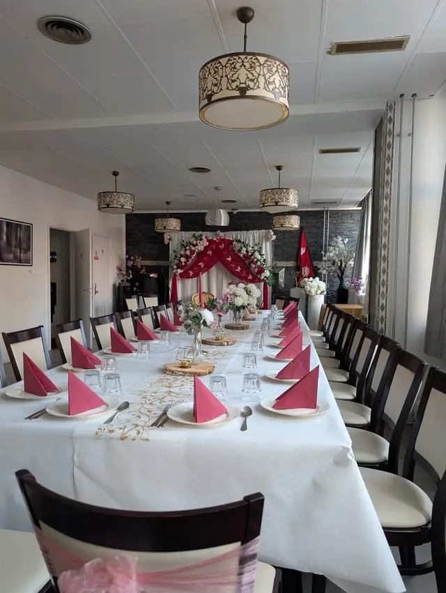 A long white-clothed table with raspberry fan napkins and a gold runner leading to a white and red draped backdrop