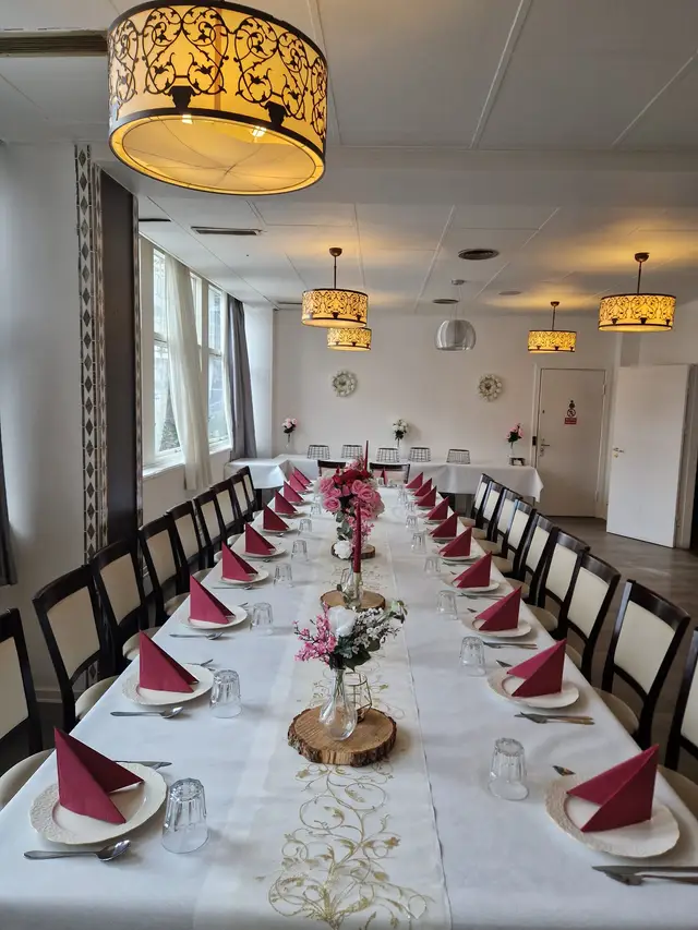 A bright room with a long table, red napkins and pink blossom centrepieces