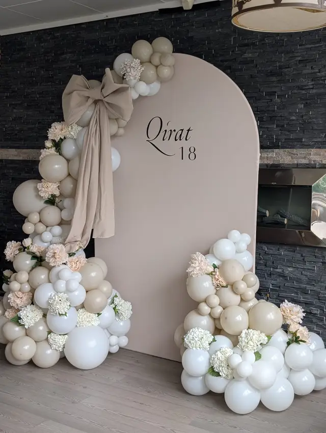 A close view of the balloon arch: cream and white balloons with hydrangeas and a draped bow