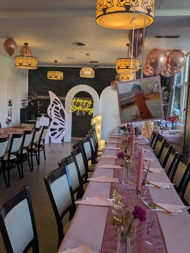 A pink themed birthday party with a butterfly arch, a lit Happy Birthday sign and a photo display
